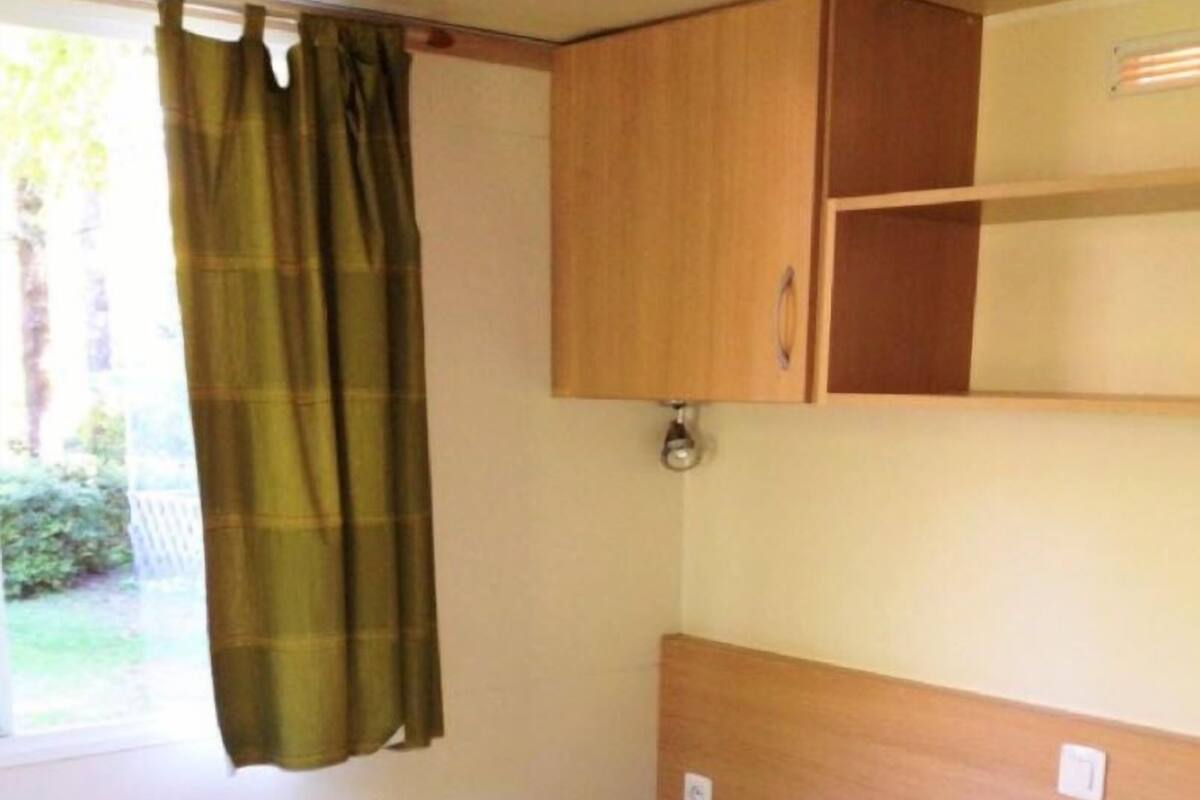 Une petite chambre avec un lit simple, une tête de lit en bois et une fenêtre avec des rideaux.