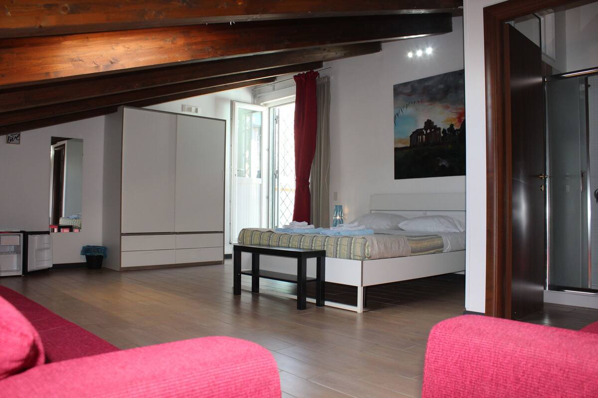 A bedroom with a bed, a bedside table, a wardrobe, and a window with curtains.
