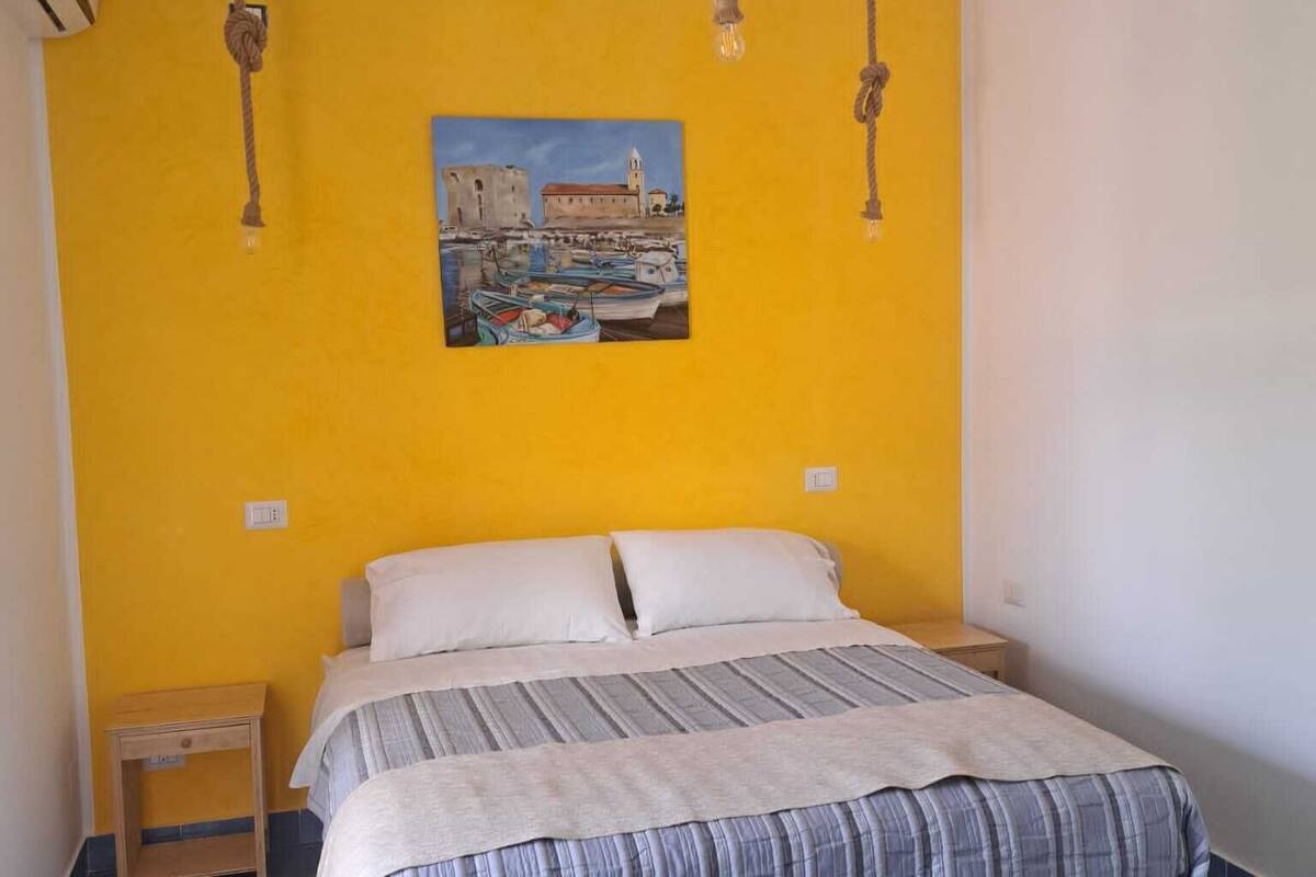 A bedroom with a bed, a nightstand, a painting on the wall, and a ceiling fan.