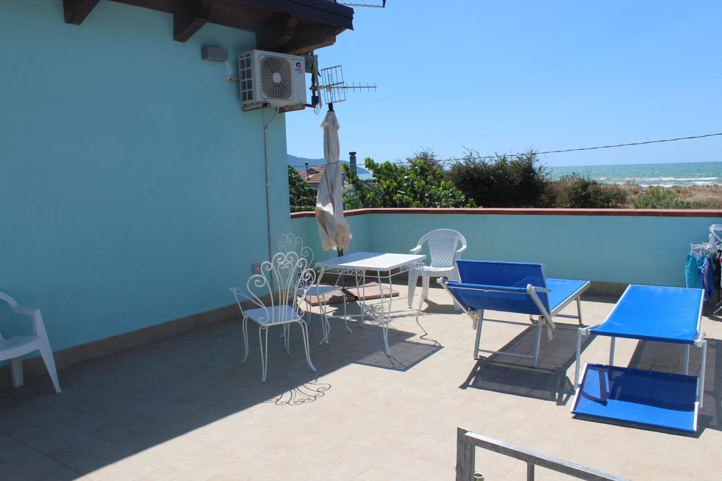 Eine Terrasse mit Tisch, Stühlen, einem Ventilator und Blick auf das Meer.