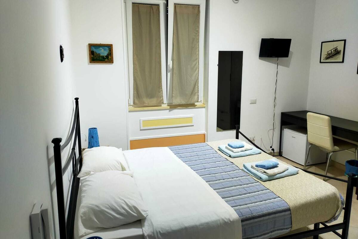 A hotel room with a bed, a desk, a chair, a TV, and a window with curtains.