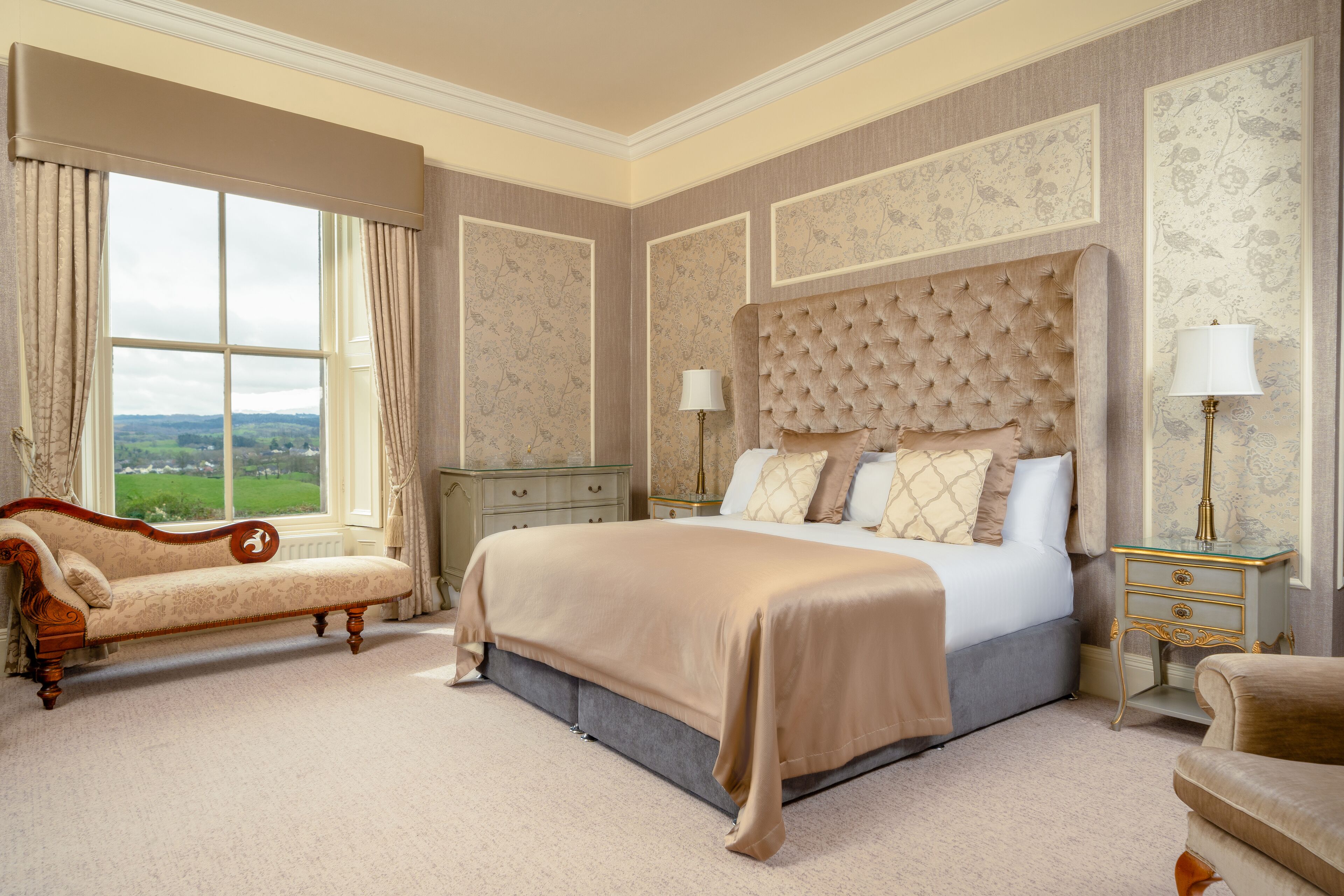 Ein geräumiges Schlafzimmer mit einem großen Bett, einer Liege und Blick auf die Landschaft durch ein großes Fenster.
