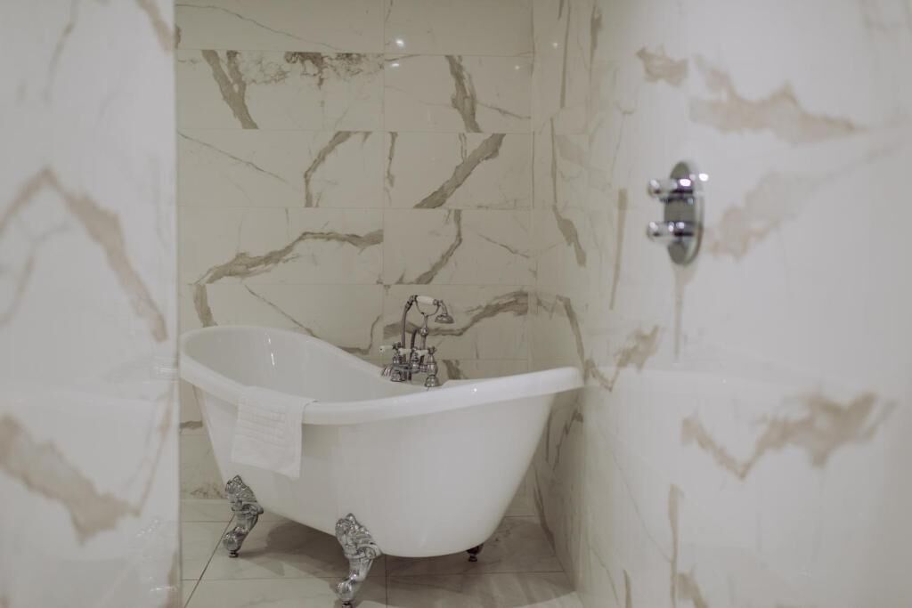 Une salle de bain avec une baignoire sur pieds, des murs en marbre et un robinet moderne.