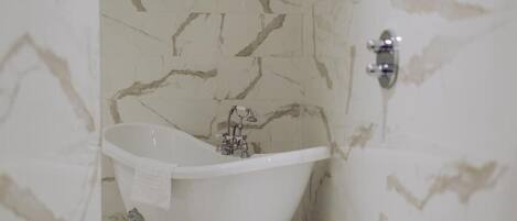 Une salle de bain avec une baignoire sur pieds, des murs en marbre et un robinet moderne.