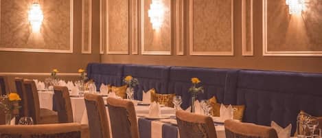 A dining area with tables set for service, a blue upholstered bench, and wall sconces.