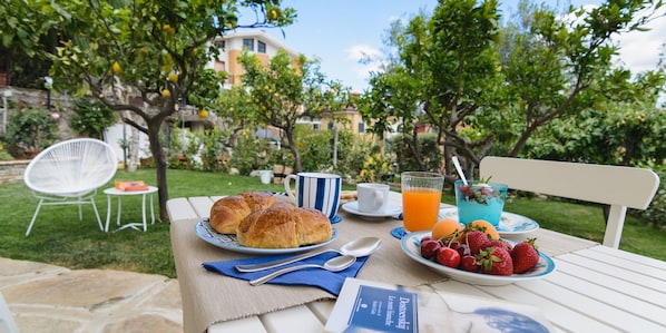 An outdoor breakfast setting with croissants, fruit, and orange juice on a table. - Casa Vittoria (Agropoli)
