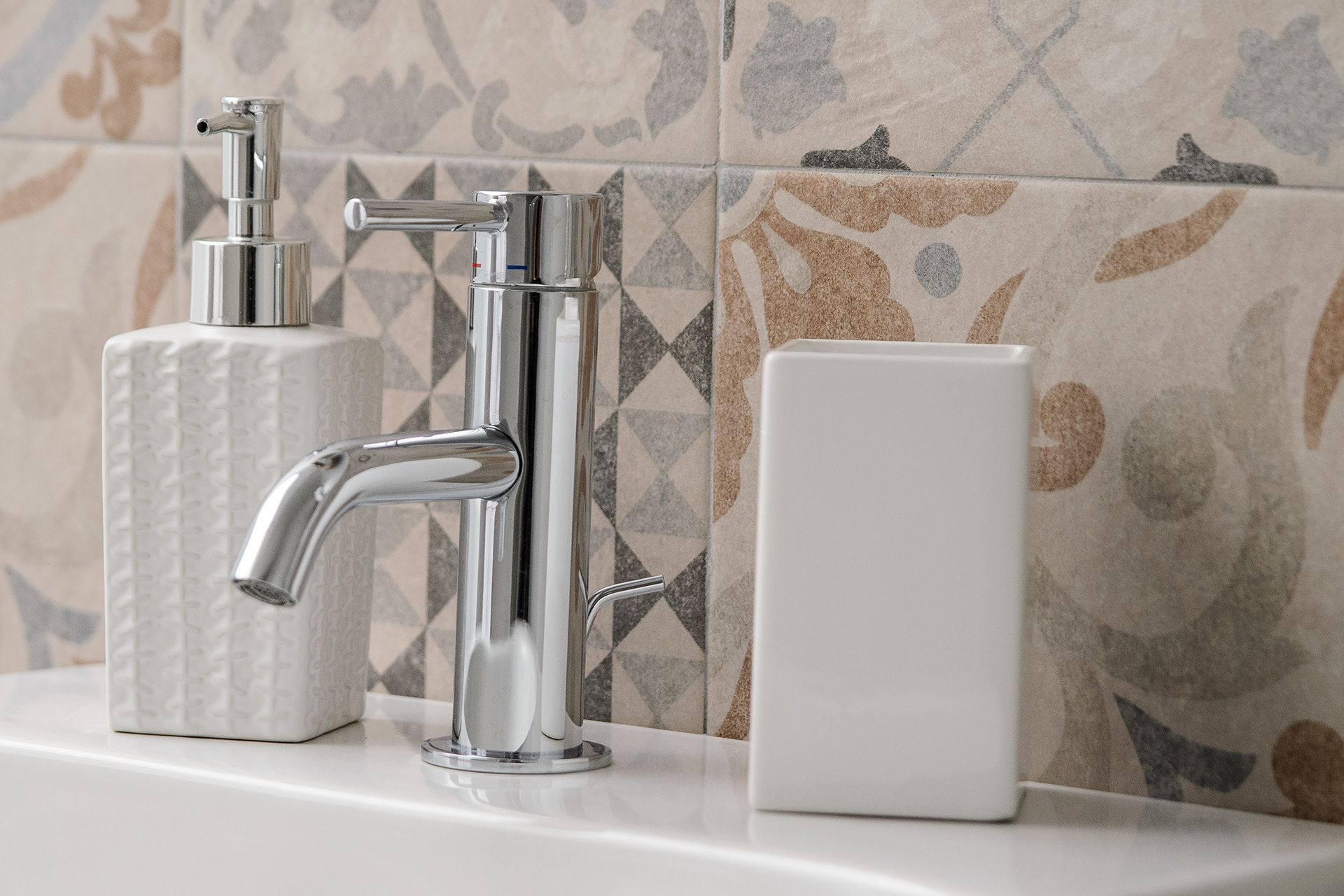 Une salle de bain avec un robinet moderne, un distributeur de savon et un récipient blanc posé sur le comptoir.