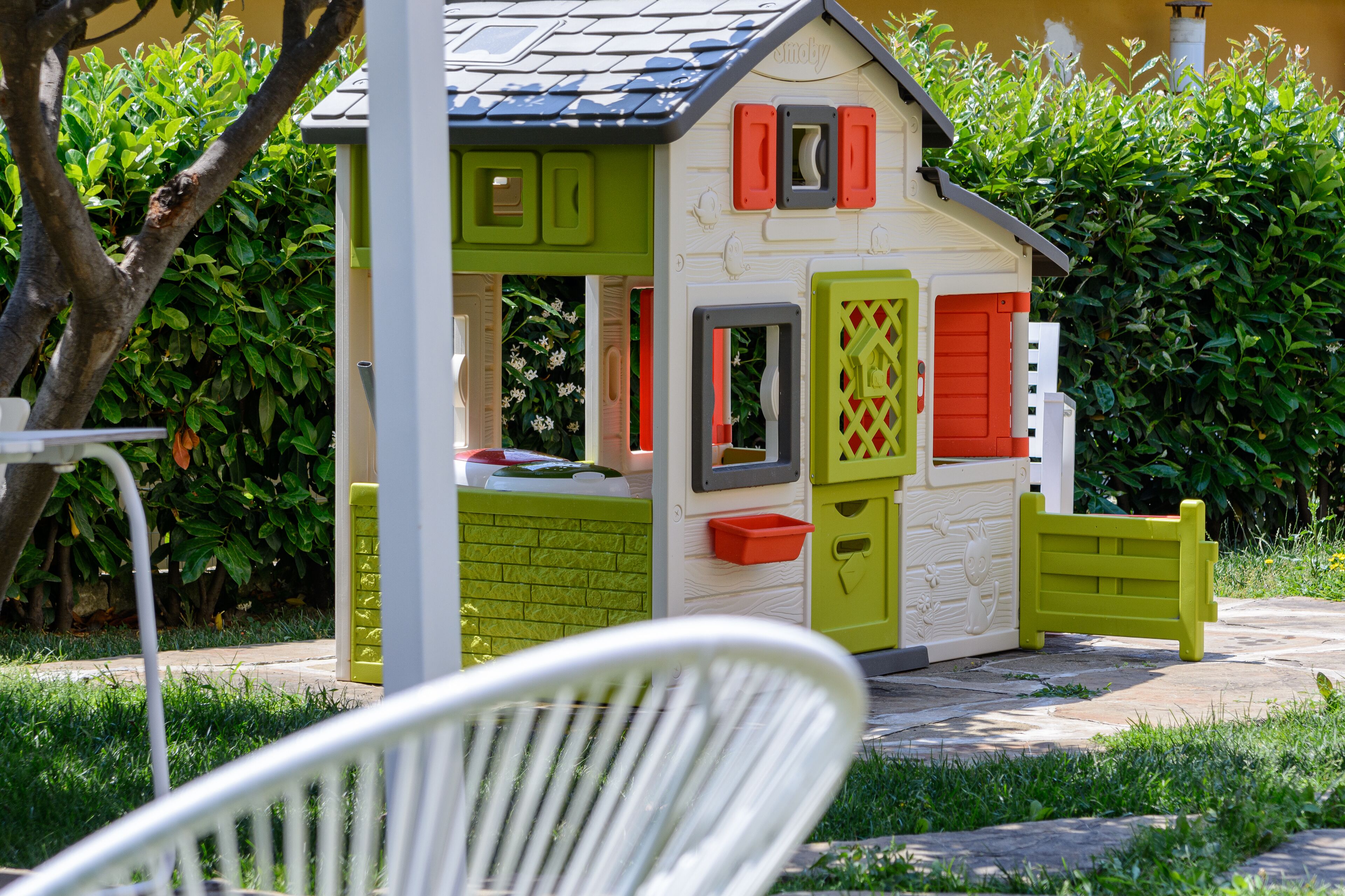 A children's playhouse with a small window, a door, and a bench outside.