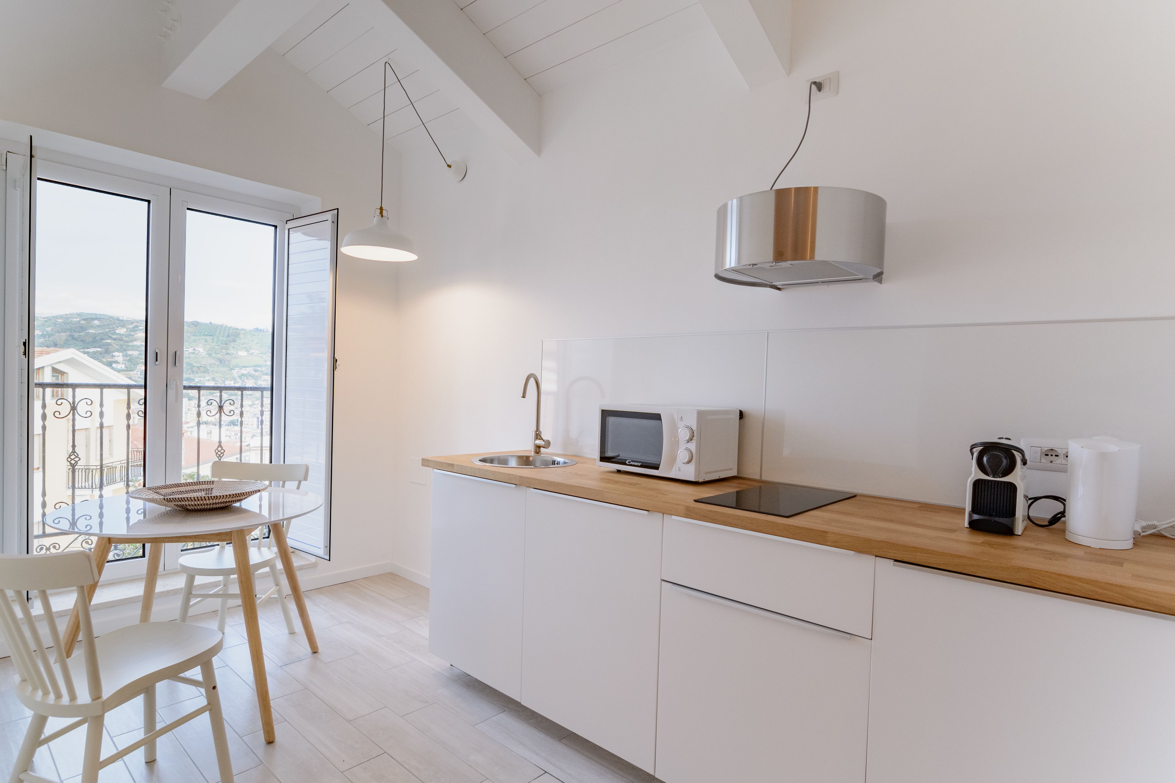 Eine moderne Küche mit weißen Schränken, einer Holz Arbeitsplatte, einer Mikrowelle, einem Wasserkocher und Blick durch große Fenster.