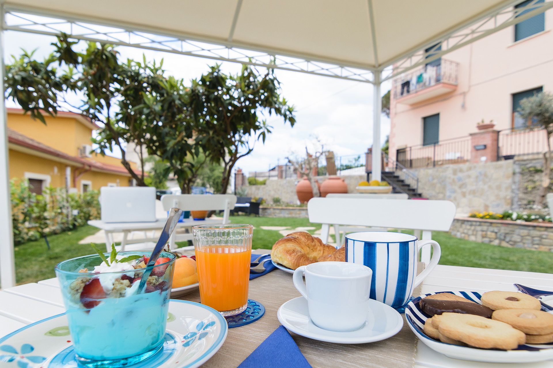 Un área de comedor al aire libre con una mesa preparada para el desayuno, que incluye un vaso de jugo de naranja, un croissant, una taza y galletas.
