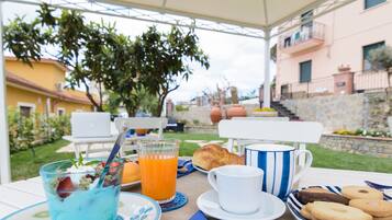Un área de comedor al aire libre con una mesa preparada para el desayuno, que incluye un vaso de jugo de naranja, un croissant, una taza y galletas.