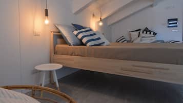Un dormitorio estilo loft con una cama de madera, dos bombillas colgantes, una mesita redonda y una silla de mimbre.