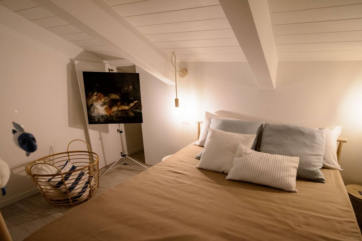 A bedroom with a bed, pillows, a TV on a stand, a wall-mounted light, and a basket.