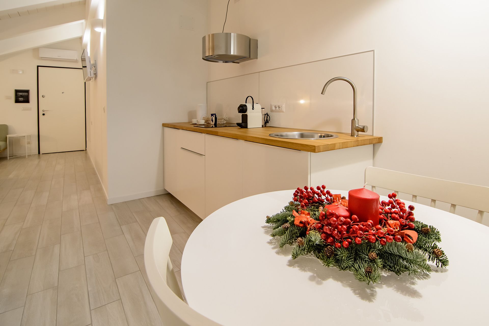 Una cocina moderna con encimera de madera, un lavamanos de acero inoxidable y una mesa de comedor blanca con un centro de mesa festivo.