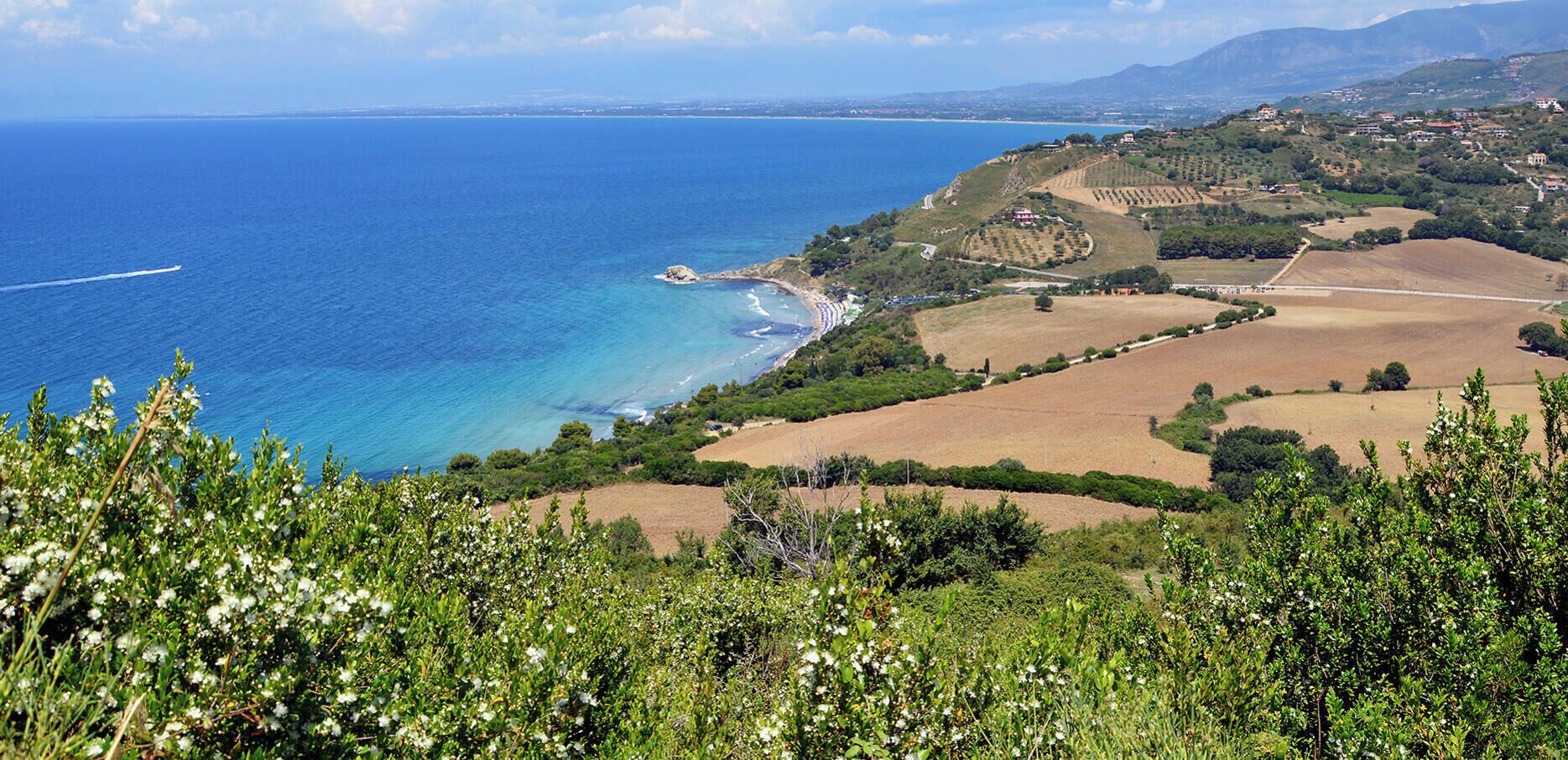 Un paisaje costero con vista despejada al mar, colinas ondulantes y un pueblo distante.