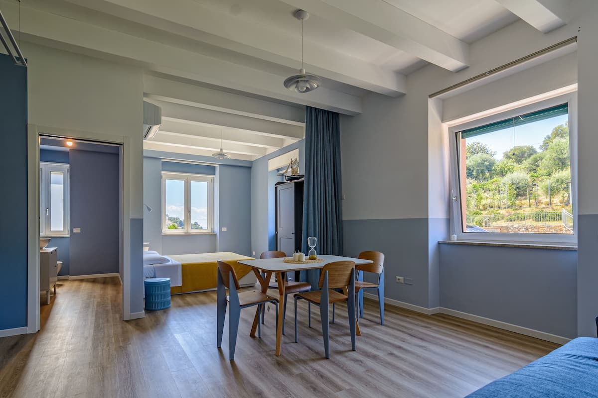 A modern room with a dining area, large windows, and a view of greenery outside.