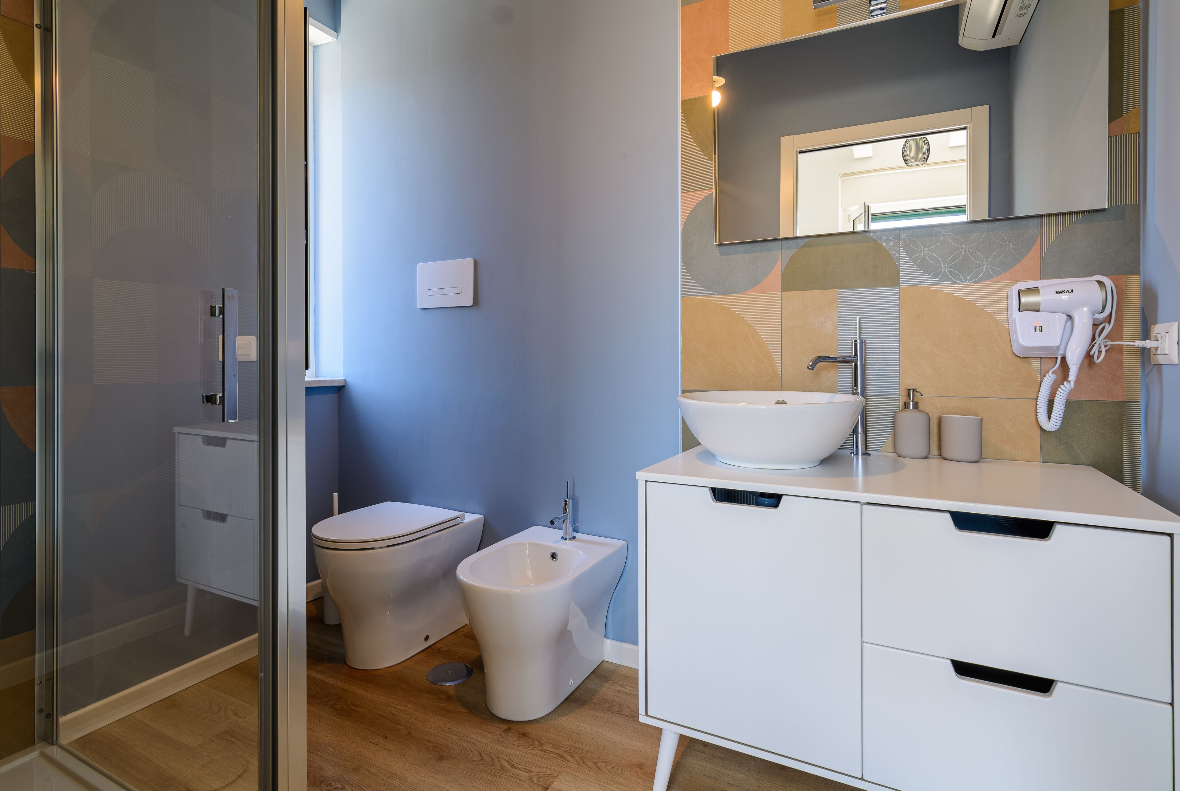 A modern bathroom with a glass shower enclosure, a toilet, a bidet, and a vanity with a sink and mirror.