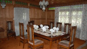A formal dining room with a large wooden table set for six, surrounded by six ornate chairs. - New Alexandra Houseboats (Srinagar)