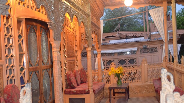 A traditional wooden room with intricate carvings, a cushioned bench, and a table with a vase of flowers. - New Alexandra Houseboats (Srinagar)