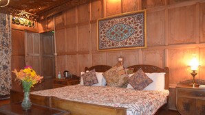 A wooden-paneled bedroom with a bed, nightstands, a vase of flowers, and a decorative wall hanging. - New Alexandra Houseboats (Srinagar)
