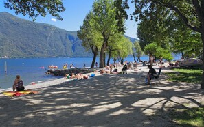 A lakeside beach with people sunbathing, swimming, and boating. - Camping Riviera (Cannobio)