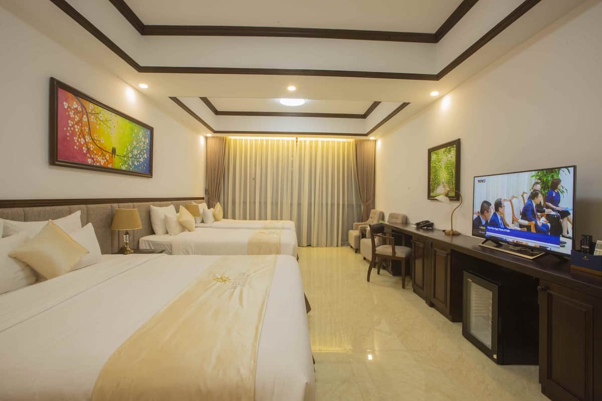 A hotel room with two beds, a desk with a television, and a seating area.