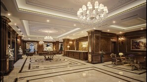 Een weelderige lobby met een imposante kroonluchter, versierde plafond en een receptiebalie.
