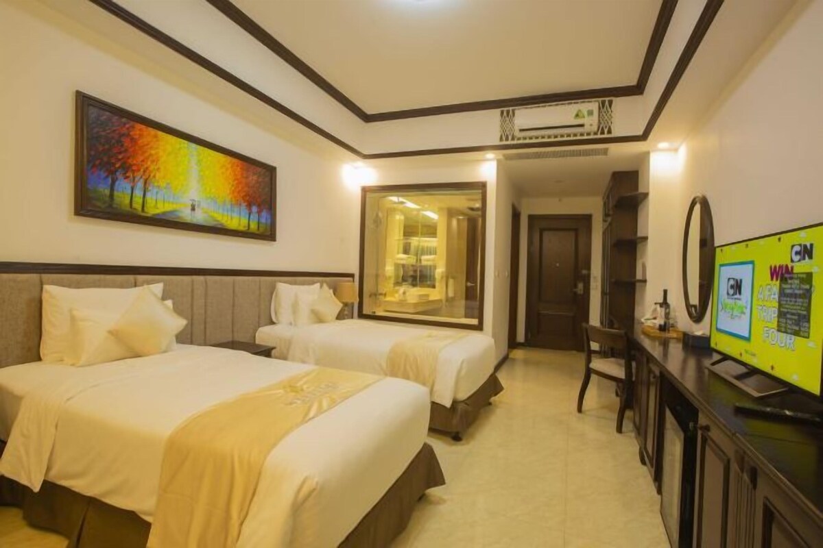 Habitación de hotel con dos camas, un cuadro en la pared, un televisor en el escritorio y un espejo.
