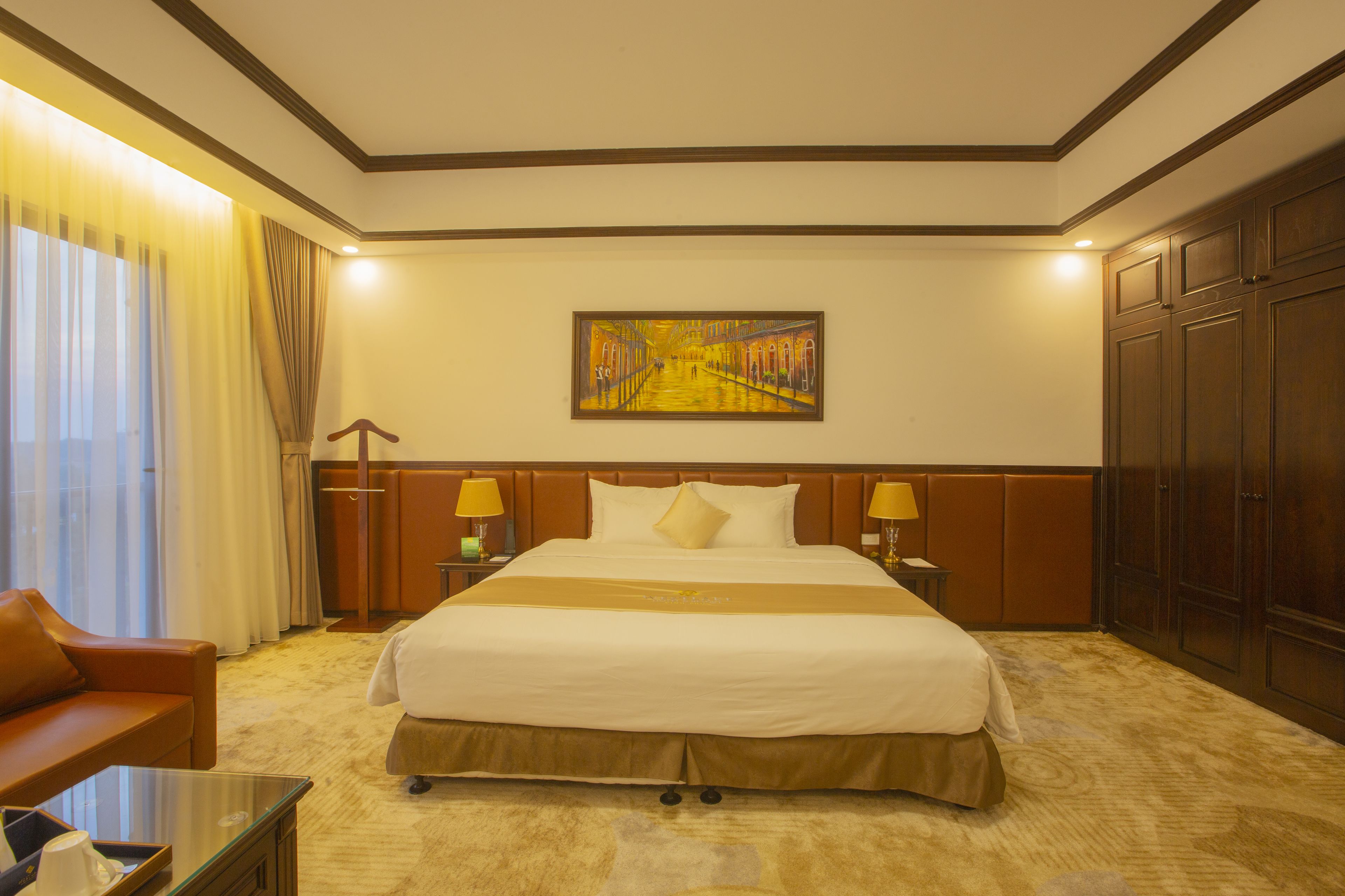 A hotel room with a large bed, two bedside tables with lamps, a sofa, and a painting on the wall.