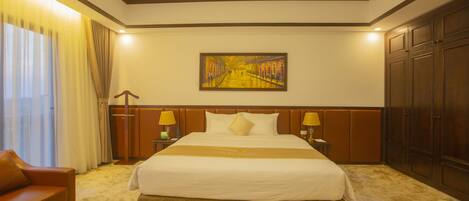 A hotel room with a large bed, two bedside tables with lamps, a sofa, and a painting on the wall.