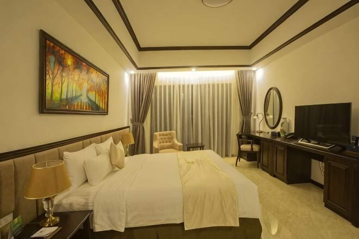 A hotel room with a large bed, a desk with a computer, a chair, a TV, and a painting on the wall.