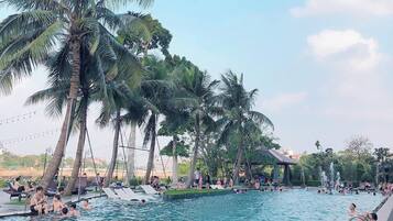 A swimming pool surrounded by palm trees, with people swimming and relaxing.
