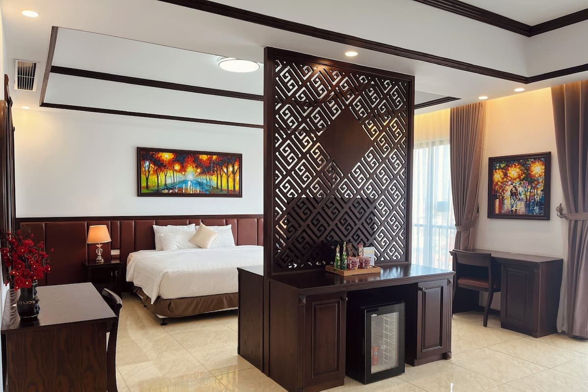 A hotel room with a bed, a desk, a minibar, and artwork on the walls.