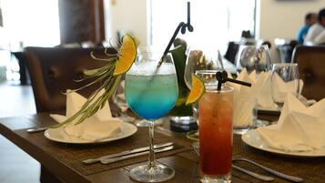 A dining table with two drinks, a green cocktail and a red drink, garnished with citrus slices and a straw.