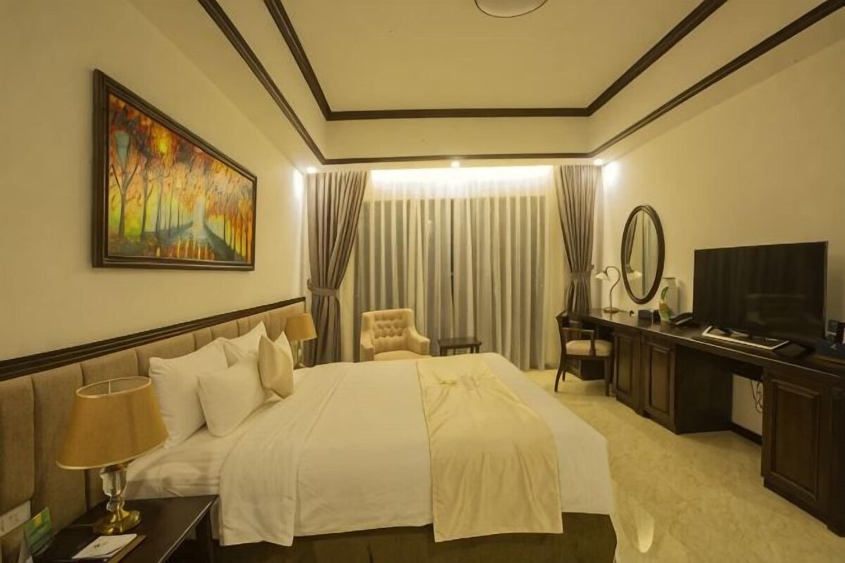 Habitación de hotel con una cama grande, un escritorio con computadora, una silla, televisor y un cuadro en la pared.