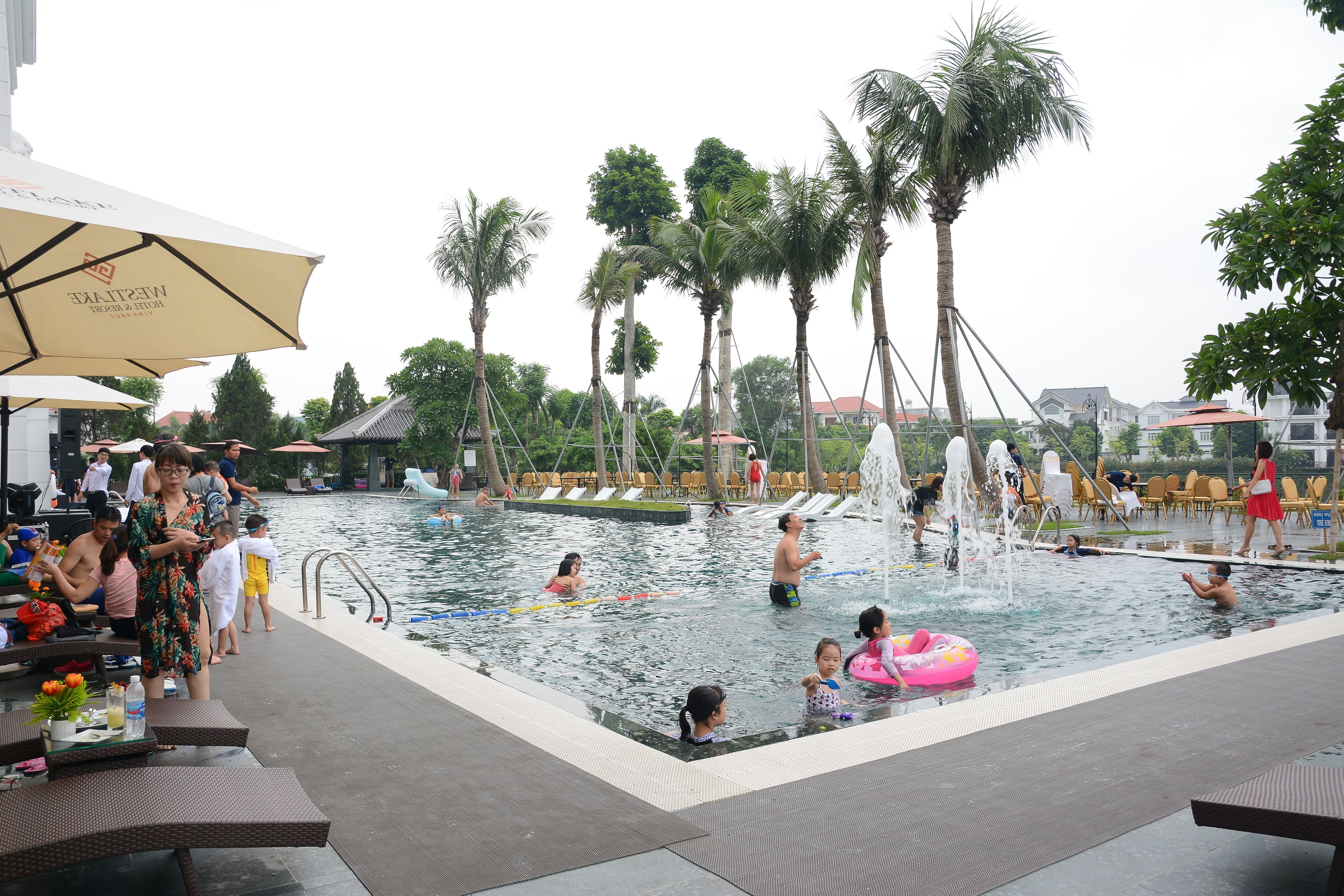 Zona de piscina con palmeras, sillas de descanso y sombrillas.
