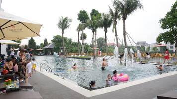Zona de piscina con palmeras, sillas de descanso y sombrillas.
