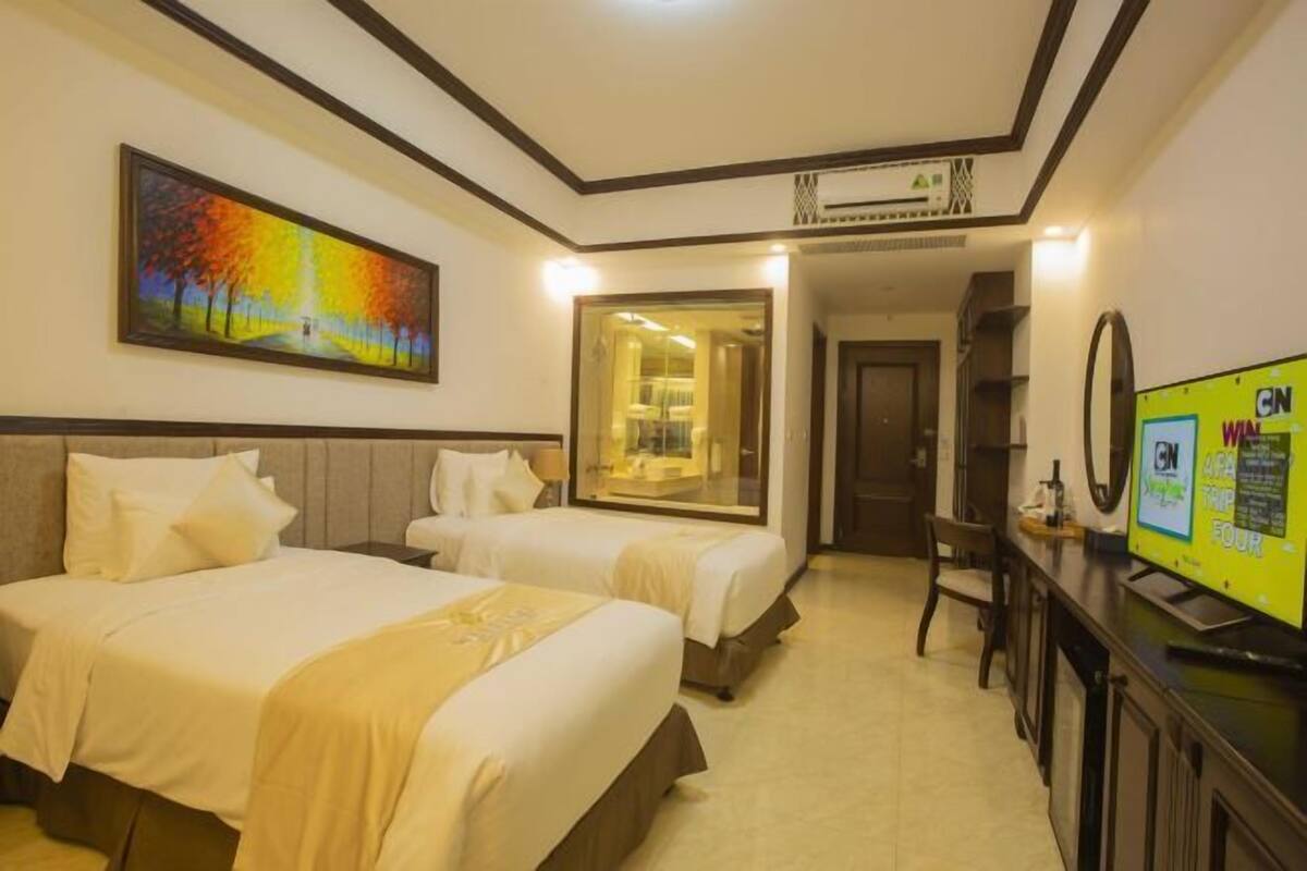 A hotel room with two beds, a painting on the wall, a TV on the desk, and a mirror.