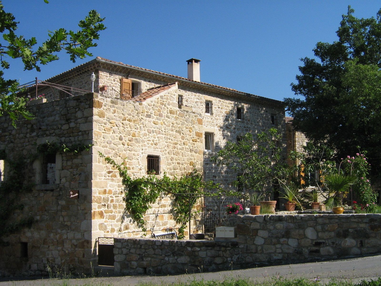 A stone building with a tiled roof, several windows, and a stone wall with potted plants.