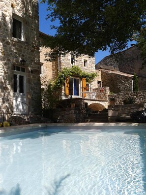 Un edificio de piedra con una piscina, un puente y un árbol en primer plano.