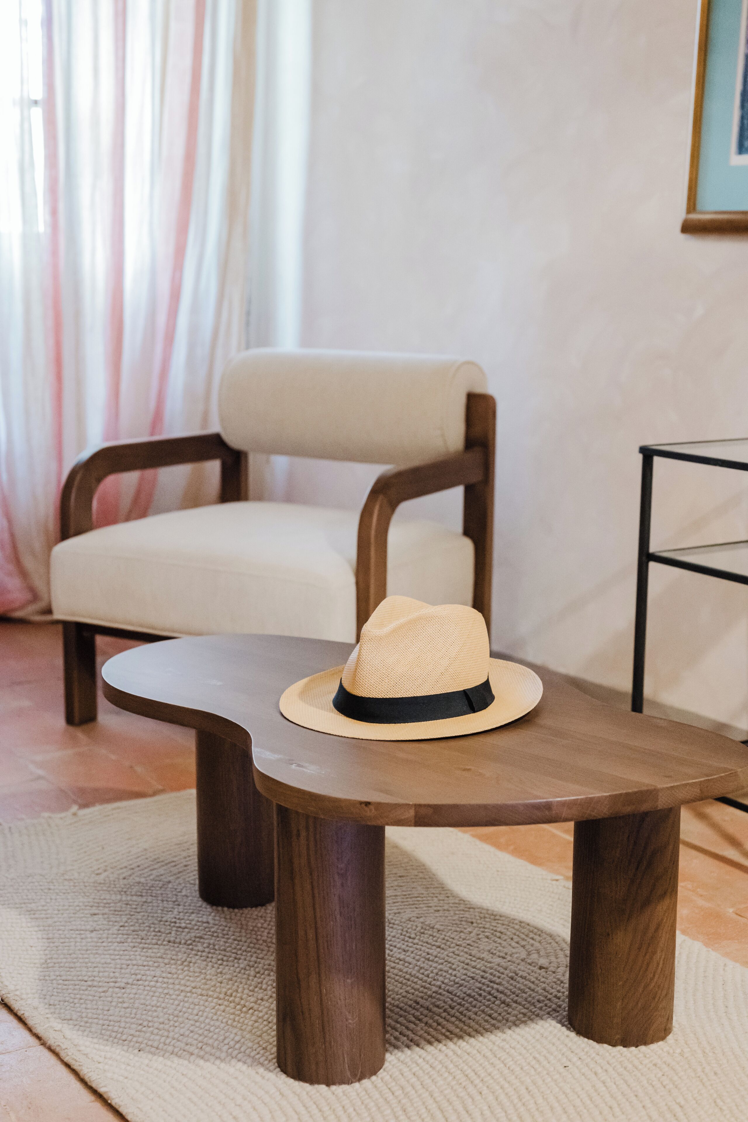 Una mesa de madera con un sombrero encima, una silla y un estante en una habitación con cortina.