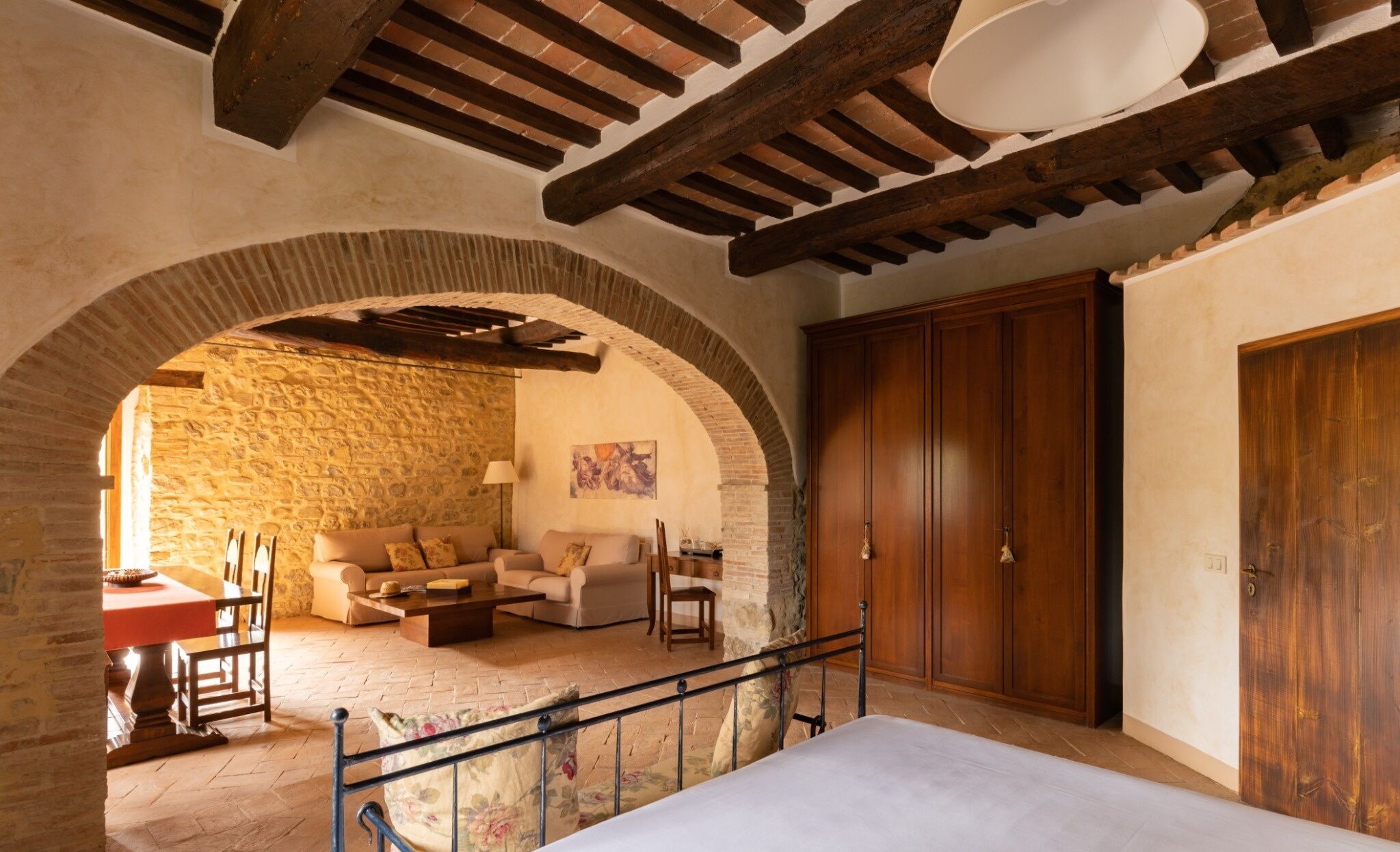 Una habitación acogedora con pared de piedra, vigas de madera en el techo, cama, sofá y armario.