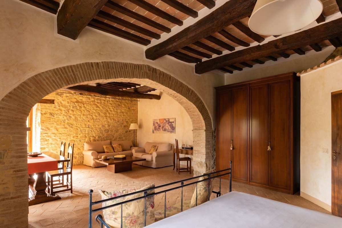 A cozy room with a stone wall, wooden ceiling beams, a bed, a sofa, and a wardrobe.