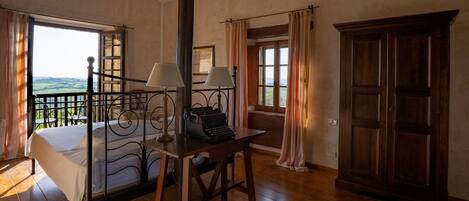 Un dormitorio con cama, un escritorio con máquina de escribir, una ventana con cortinas y vistas al exterior.