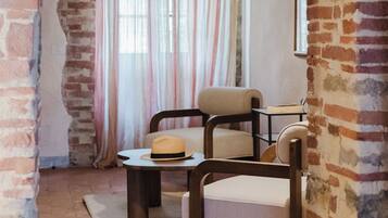 A room with exposed brick walls, a wooden ceiling, a large window with curtains, a chair, a table, and a hanging lamp.