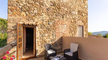 Un edificio de piedra con puerta de madera, dos sillas de mimbre y una mesa con una revista.