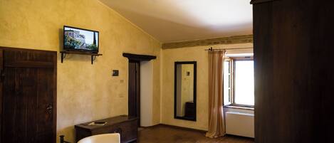 Habitación de hotel con cama, una silla, televisor, ventilador de techo, ventana con cortinas y un armario de madera.