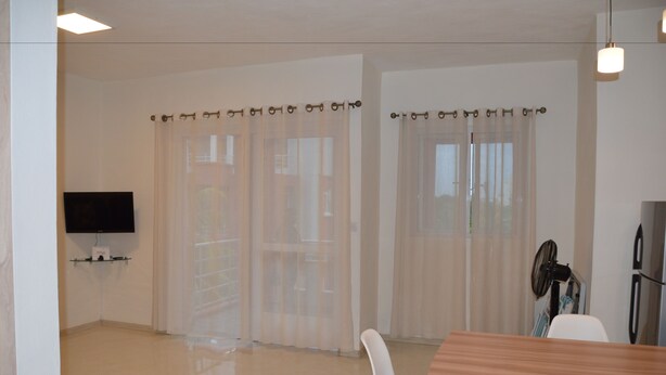 A modern, well-lit room with a wooden dining table, white chairs, a flat-screen TV mounted on the wall, and a ceiling fan. - AZ New Pereybere Beach Apartment (Grand-Baie)