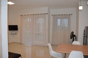 A modern, well-lit room with a wooden dining table, white chairs, a flat-screen TV mounted on the wall, and a ceiling fan. - AZ New Pereybere Beach Apartment (Grand-Baie)