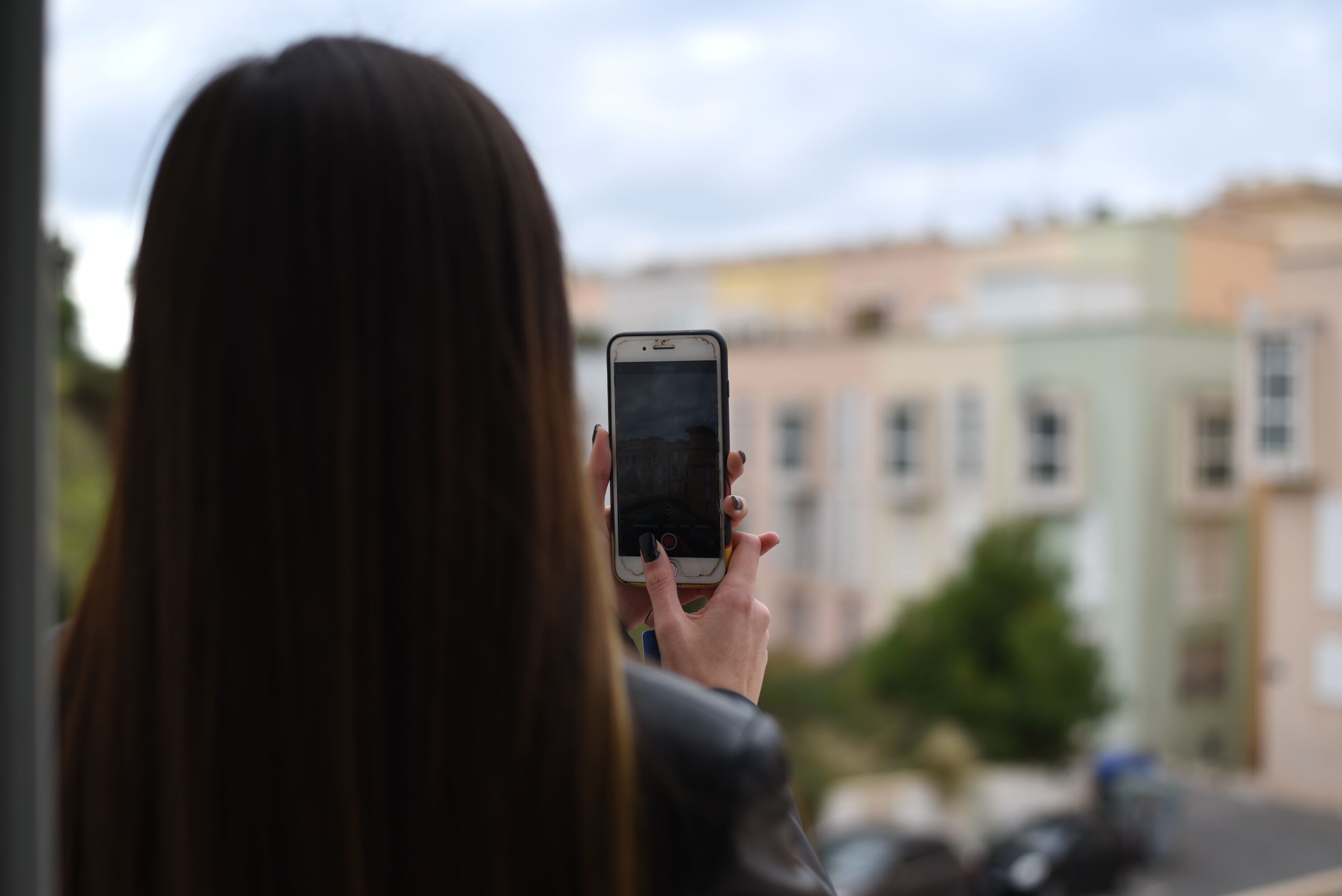 A person holding a smartphone, facing a row of buildings.